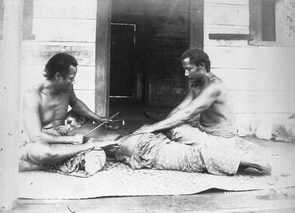 Un tatoueur Samoan, Tufuga ta tatau et son assistant (à droite), exécutant un tatau traditionnel sur le dos d'un homme. Le tatoueur utilise des outils traditionnels. 1895 @Thomas Andrew